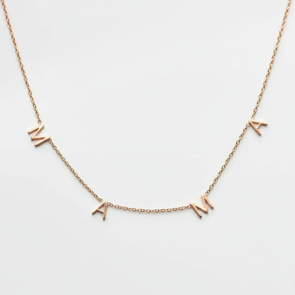 A delicate gold chain necklace featuring three small letter charms spelling 'MAMA' in gold, displayed against a clean white background.